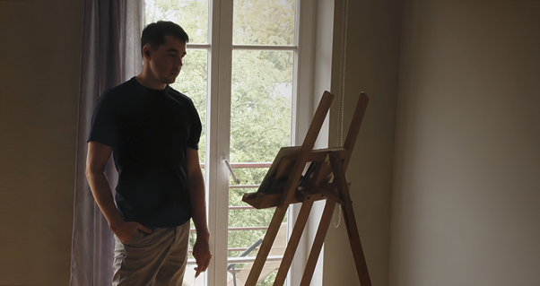 Kait Kübar standing beside a canvas on an easel in the studio